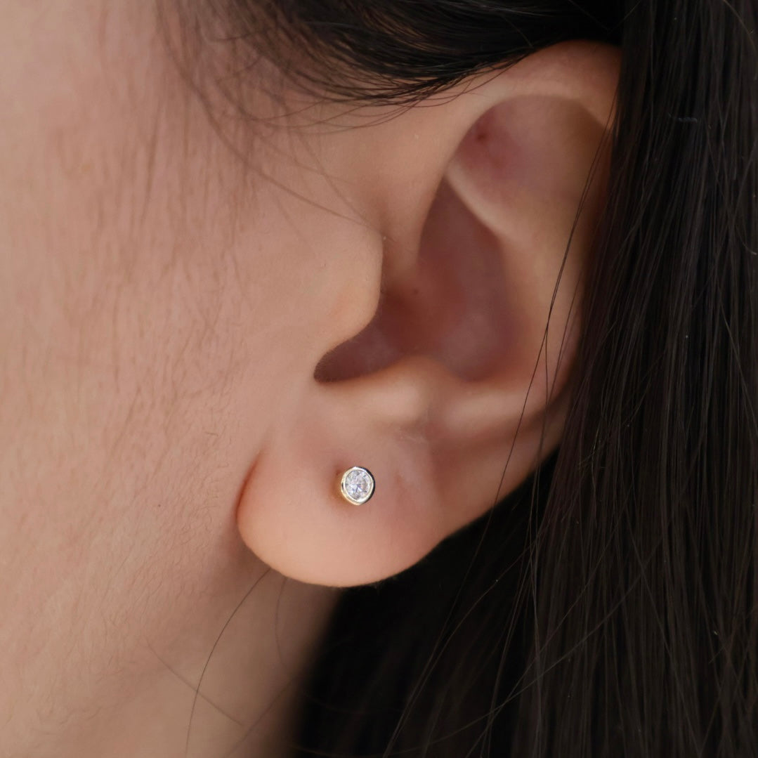 Close-up of an ear wearing a diamond stud earring with dark hair partially visible.