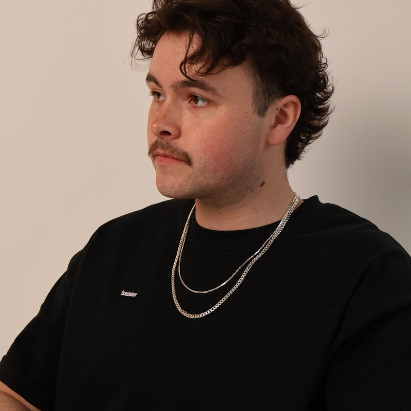 Man wearing a black t-shirt with a subtle logo, sitting against a plain background