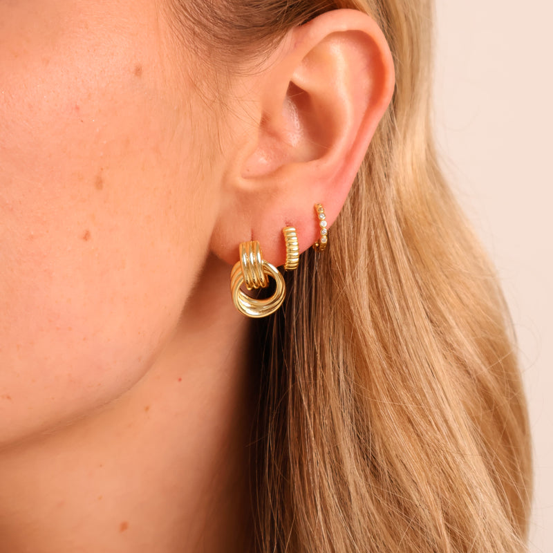Close-up of a person wearing gold hoop earrings with a plain background